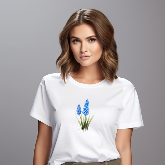 Moteriški marškinėliai “Žydrė” – balti, puošti subtiliais mėlynais pakalnutės žiedais, spinduliuoja ramybe ir švara.